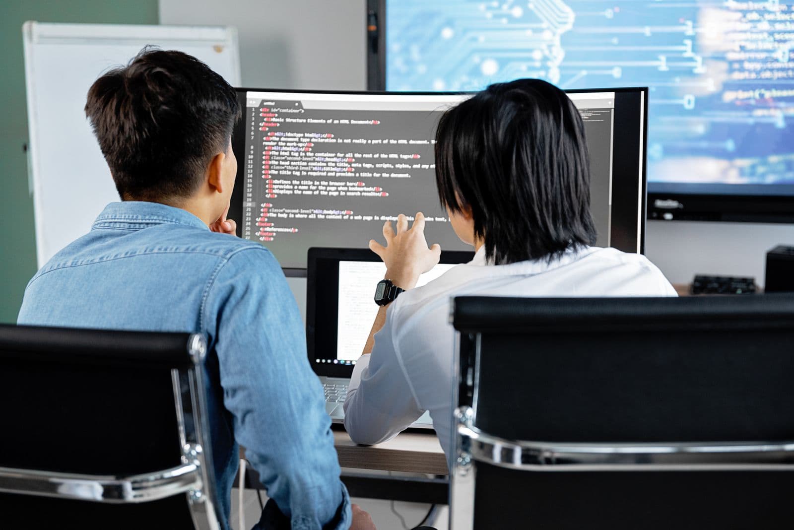 Deux personnes de dos relisent du code sur un grand écran