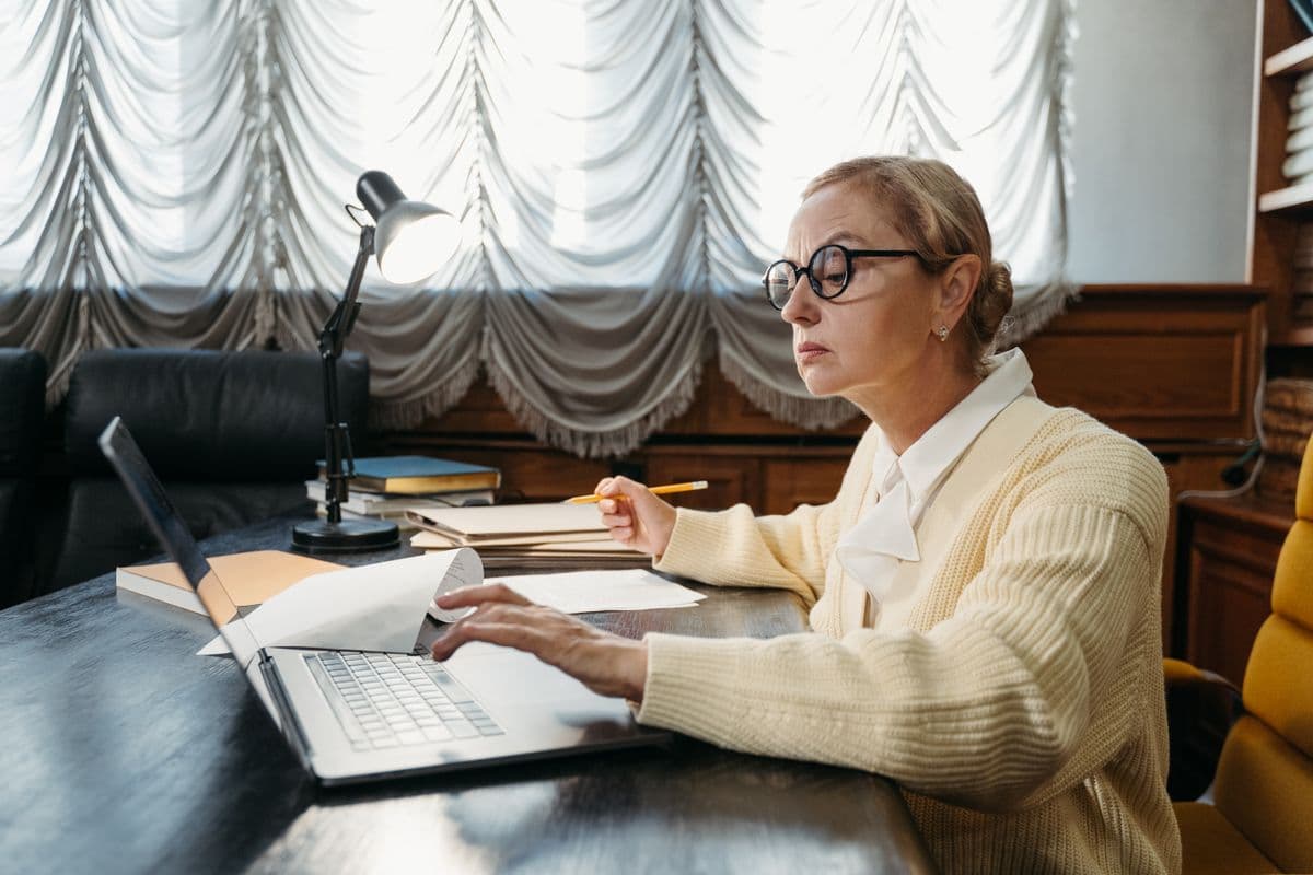 Une femme rédige sur son ordinateur portable, concentrée, à son bureau